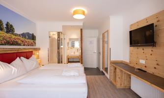 A bright hotel room with a large bed and decorative pillows. The walls are partially made of wood, and there is a television as well as a modern bathroom.
