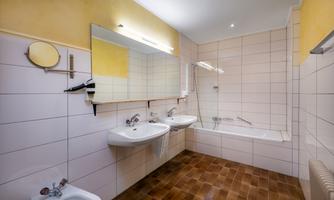 A modern bathroom with two sinks and a bathtub. The walls are brightly tiled, and there are large mirrors above the sinks.