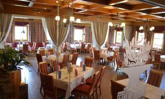 A cozy restaurant with light wooden furniture and elegant table decoration. Large windows provide plenty of natural light and an inviting atmosphere.