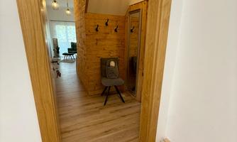 A bright entrance area with wooden doors and a modern wooden chair. The floor is laid with light laminate, and there is attractive lighting.
