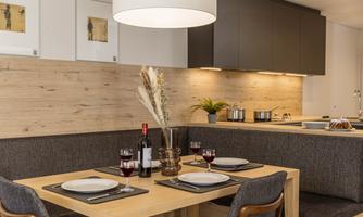 A modern kitchen with a cozy dining area. The table is set for four people and there are wine and plants on the table.