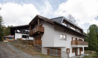 Two modern houses in a rural setting. The buildings have balconies and are surrounded by trees.