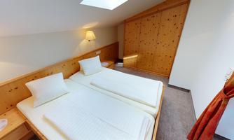 A cozy bedroom with two beds and wooden details. The room has window light and a warm atmosphere.