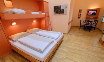 A cozy room with a double bed and an adjustable-height bed above. The room has wooden floors and a seating area with a table and chairs.