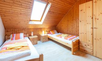 A cozy bedroom with two single beds and wooden paneling. A skylight lets in plenty of daylight.