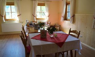 A bright dining room with a large table and chairs. On the table, there is a red tablecloth and fresh flowers in the center.