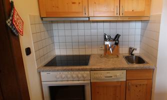 A small kitchen with wood-colored cabinets and a bright countertop. It is equipped with a stove, an oven, and a sink.