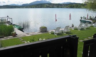 A tranquil lake with a beautiful shore, loungers, and boats. In the background, rolling landscapes and a cloudy sky can be seen.