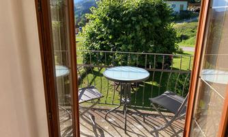 A beautiful balcony with a table and two chairs. In the background, you can see a lot of green grass and trees.