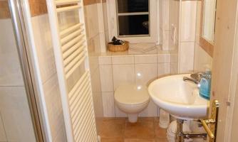 A modern bathroom with a shower, sink, and toilet. The walls are tiled and there is a small window for daylight.