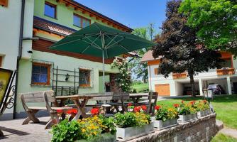 A beautiful outdoor area with a large table and a sunshade. Colorful flowers adorn the surroundings, and a green lawn provides space to relax.