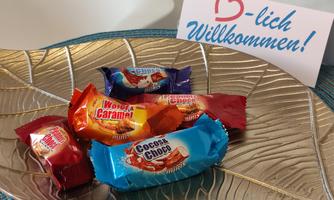 A silver bowl with colorful candy wrappers inside. A welcome sign in German is also visible.