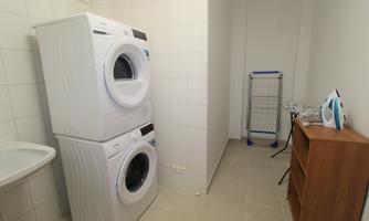 A modern laundry room with a washing machine and a dryer stacked on top of each other. Additionally, there is a clothes drying rack and an ironing board.