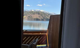 View from a balcony overlooking a tranquil lake and snow-covered mountains in the background. A comfortable armchair is visible in the foreground.