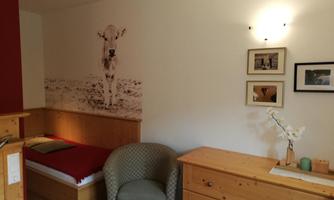 A cozy room with wooden furniture and an animal picture on the wall. There is an armchair, a bed, and decorative frames.