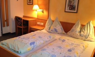 A cozy bedroom with a double bed and colorful bedspreads. In the room, there is a chair and a bedside lamp.