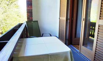 A balcony with a table and chairs. The view features green trees and plenty of daylight.