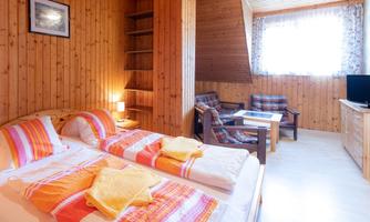 A cozy room with wooden paneling and two single beds. There is a window with plenty of natural light and a seating area with a table.