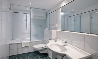 A modern bathroom with white tiles and a large mirror wall and bathtub.
