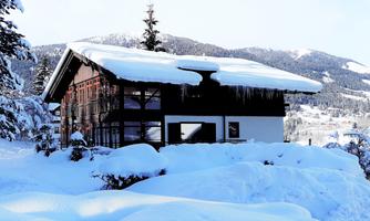 A cozy house in winter, surrounded by snow and fir trees. The landscape is picturesque and peaceful.