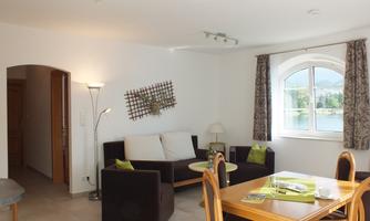 A modern living room with a cozy sofa and a wooden table. The room has large windows and is bright and friendly.