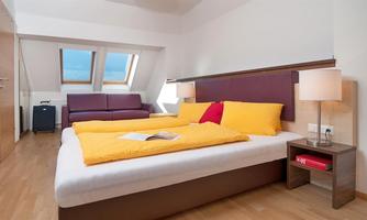 A cozy room with a large bed and bright yellow tones.  
Windows with a view and a seating area create a pleasant atmosphere.