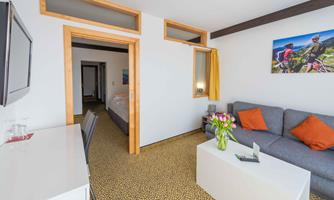 A modern room with a cozy sofa, a table, and colorful decorations. In the background, you can see a sleeping area and a picture of cyclists on the wall.