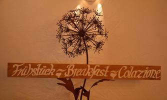 A decorative sign with the inscription "Frühstück - Breakfast - Colazione" is hanging on the wall. In the background, a stylized flower can be seen.