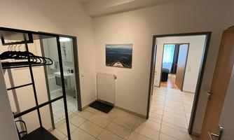 A bright hallway with tiled flooring and an open coat rack. A picture on the wall and access to other rooms can be seen.