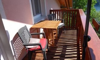 A cozy balcony with a table and two chairs. The sun is shining and there is a lot of wood and some greenery in the surroundings.
