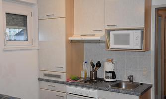 A modern kitchen with light cabinets and a microwave. Kitchen utensils and a coffee machine are on the countertop.