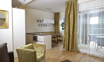 A modern furnished living kitchen with wooden floor and large windows. In the foreground, there is a cozy chair and a dining table.