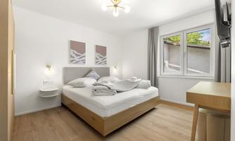 A bright bedroom with a double bed and modern furniture. The room has a window that lets in natural light.