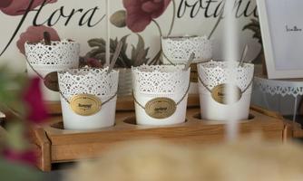 Several white pots with decorative tops and labels are on a wooden tray. In the background, floral motifs can be seen.