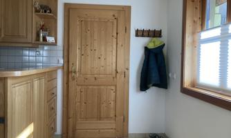 A simple entrance area with a wooden door and a hook for jackets. A few shoes are on the floor and the walls are painted light.