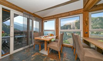 An inviting dining area with wooden furniture and large windows that showcase a beautiful mountain landscape. The table is set with fresh breakfast and a view of nature.