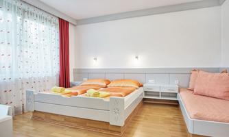 A bright bedroom with a large double bed and an additional sleeping area. The walls are in neutral colors, and the windows let in plenty of light.