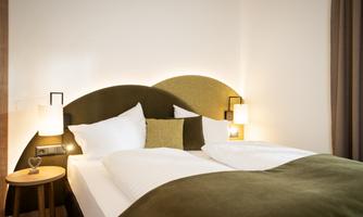 A modern bedroom with a comfortable double bed and soft lighting. The decoration in green and beige tones creates a cozy atmosphere.