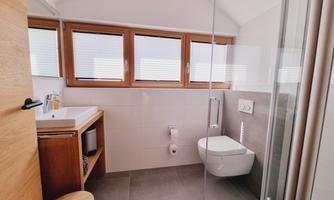 A modern bathroom with a shower and wooden details. The large windows provide plenty of natural light.