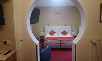 A cozy hotel room with a comfortable double bed and red pillows. The room has a modern TV and pleasant lighting.