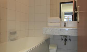 A modern bathroom with a bathtub and a sink. The room has bright tiles and a large mirror area.