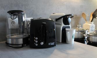 A modern kitchen corner with a kettle, a toaster, and a coffee machine. There are also some cooking utensils on the countertop.