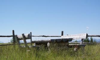 A wooden log with a fence in a meadow. The sky is clear and blue.