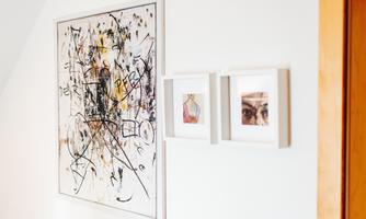 A modern, abstract painting with vibrant colors hangs on the wall. Next to it are two smaller pictures in white frames.