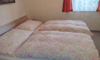 A simple bedroom with a double bed and two large, colorful bed covers. In the background, curtains and a window are visible.