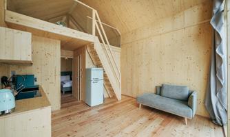 A modern wooden house with an open living area. The decor is bright and minimalist, with a staircase leading to a sleeping area.