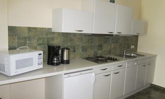 A modern kitchen with white cabinets and a dark tiled wall. On the countertop, there is a microwave, a coffee machine, and a stove.