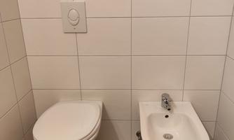 A modern bathroom with toilet and bidet. The walls are tiled with white tiles.
