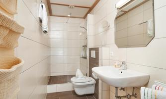 A modern bathroom with bright tiles and a shower. There is a sink and a toilet, as well as towels and a laundry basket.