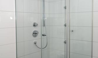 A modern glass shower cabin with shiny fixtures. The walls are clad in white tiles, and the floor is tiled in dark color.